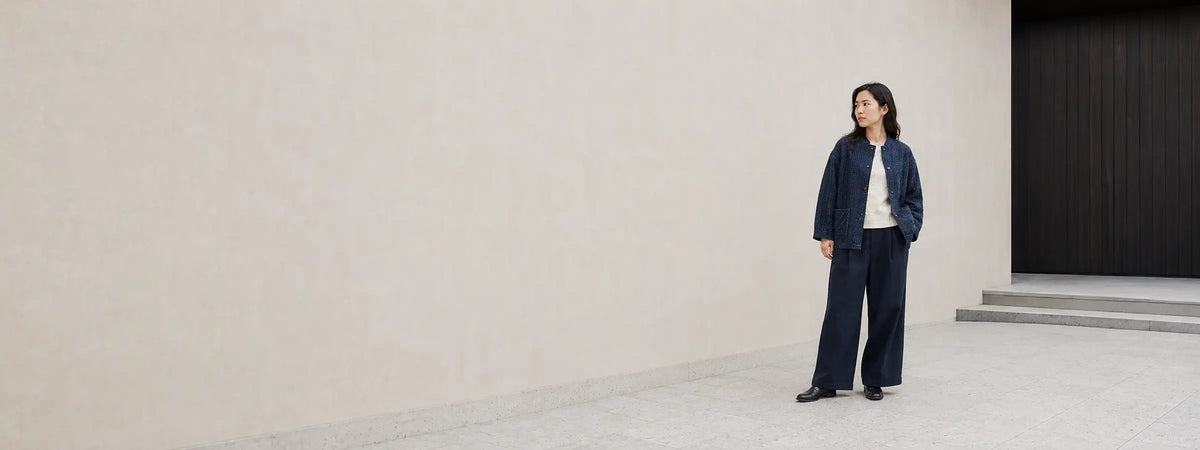 Femme portant une veste en indigo texturé et un pantalon ample devant une architecture japonaise minimaliste.