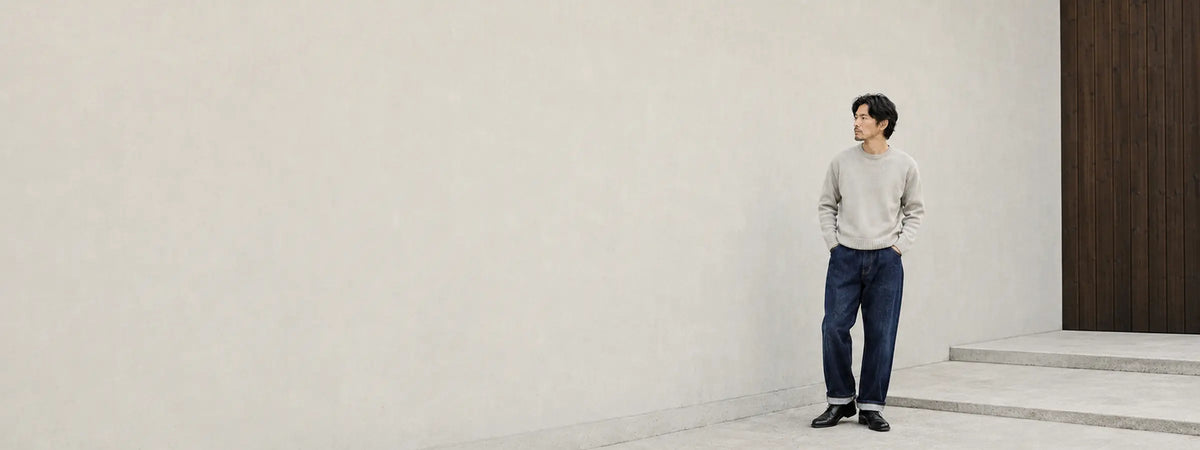 Homme portant un jean japonais ample en denim indigo avec revers devant une architecture minimaliste.