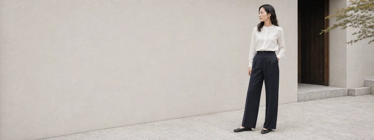 Femme portant un pantalon ample bleu nuit à taille haute devant une architecture japonaise claire et épurée.