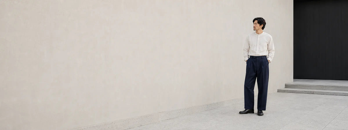 Homme portant un pantalon ample bleu nuit en sergé devant une architecture japonaise minérale et épurée.