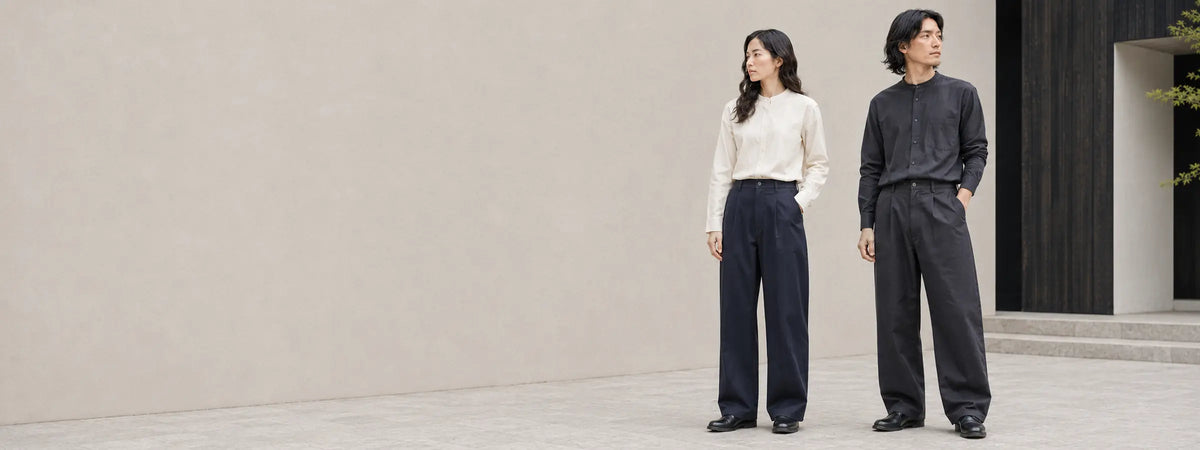 Deux mannequins portant des pantalons japonais amples bleu nuit et anthracite devant une architecture claire.