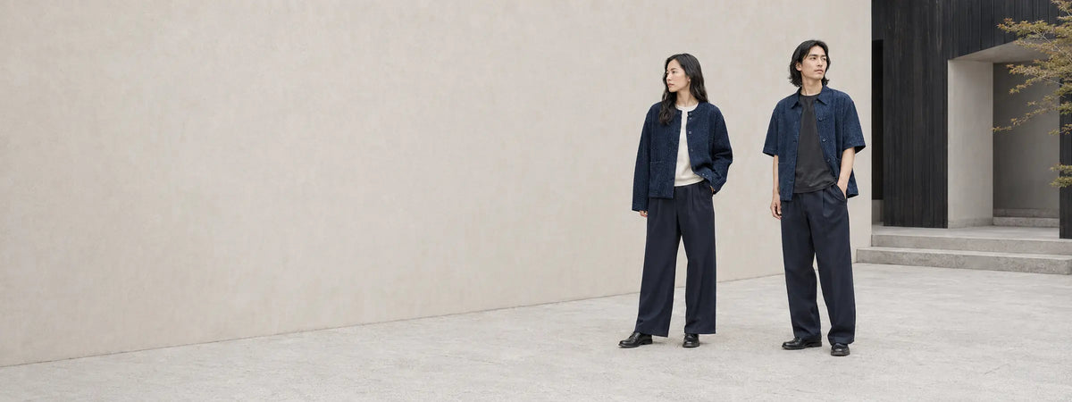 Deux mannequins portant des vestes indigo et des pantalons amples devant une architecture japonaise minimaliste.