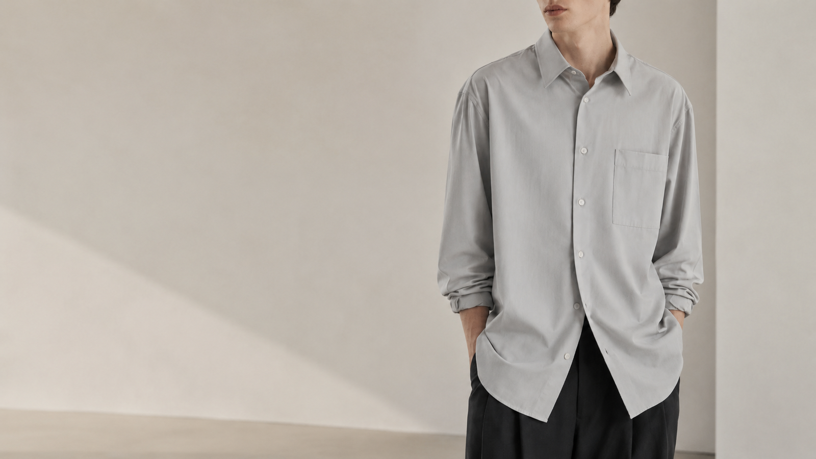Homme portant une chemise Dunst gris clair à coupe ample avec pantalon noir dans un décor studio minimaliste, style mode coréenne homme.
