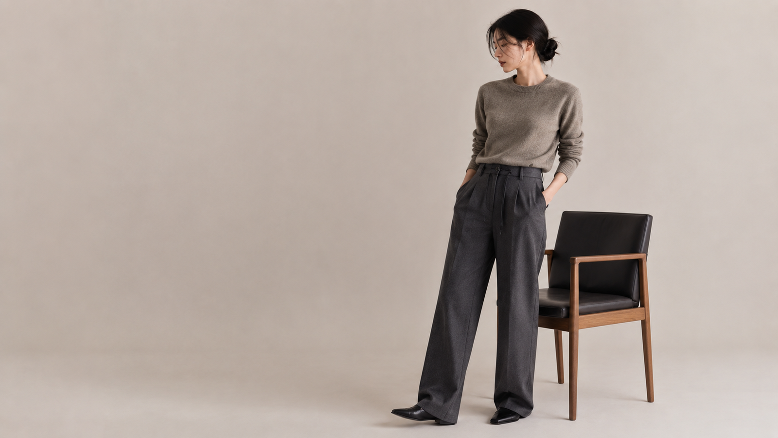 Femme portant un pantalon ample Dunst gris foncé avec maille neutre dans un décor studio minimaliste, style mode coréenne femme.